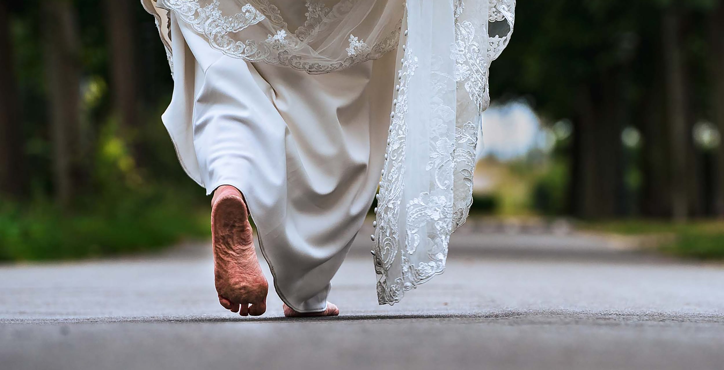 Bruid op blote voeten met kanten sleep over een landweg in Limburg – spontane trouwfoto